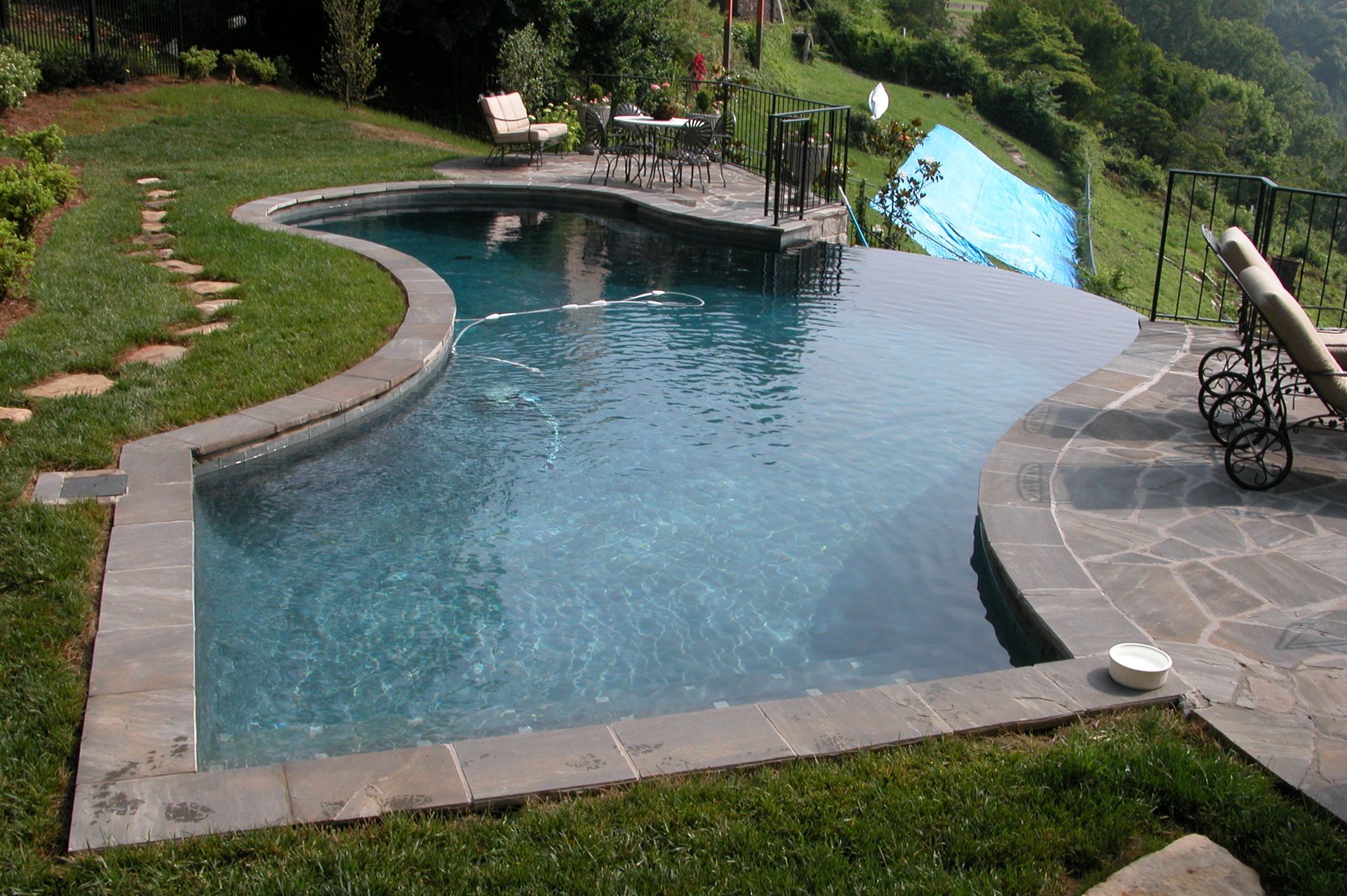 Backyard swimming pool with curved stone deck, blue water, and lounge chairs
