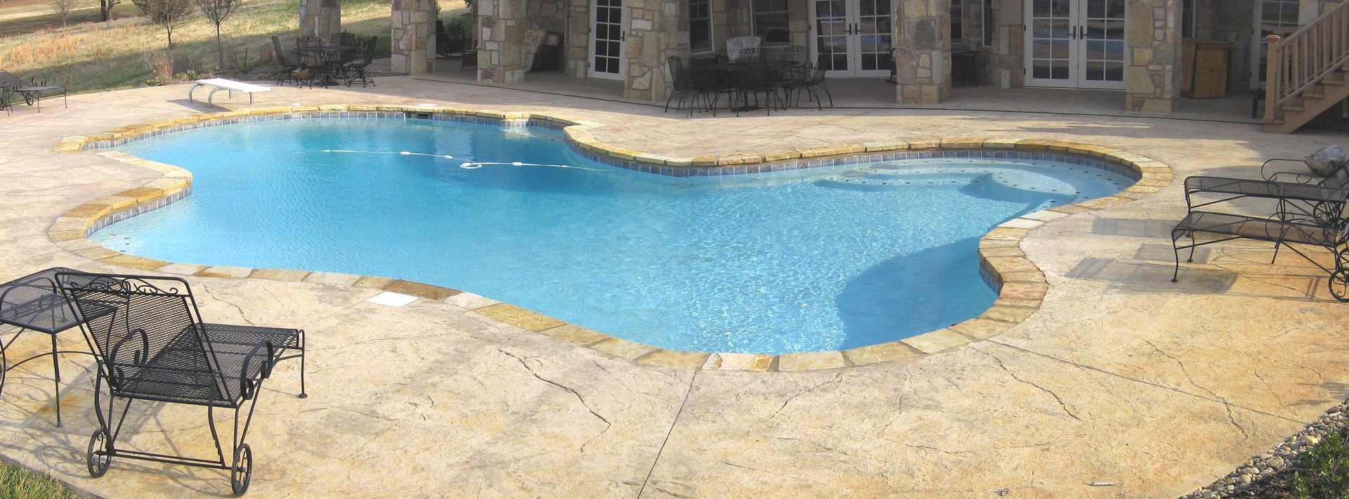 Backyard swimming pool with patio chairs and stone decking, seen in daylight