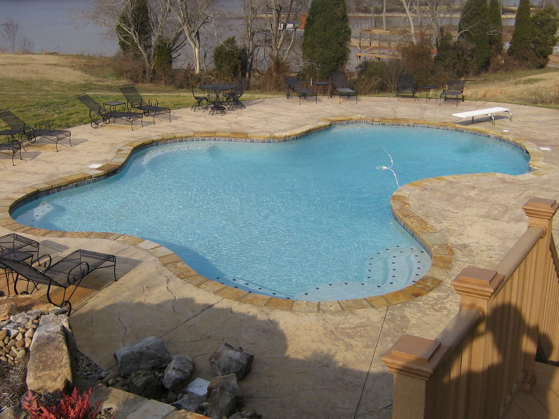 Outdoor swimming pool with blue water, stone deck, and lounge chairs in a backyard setting