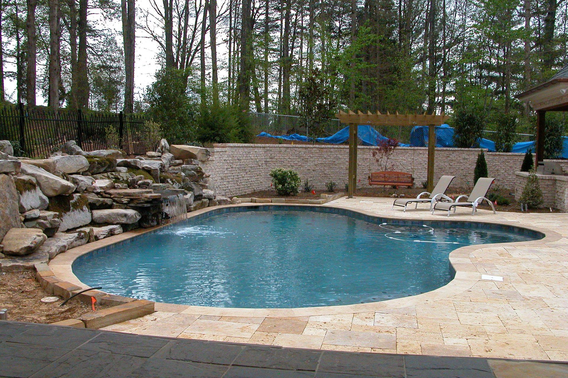 Backyard pool with stone patio, lounge chairs, and trees in the background