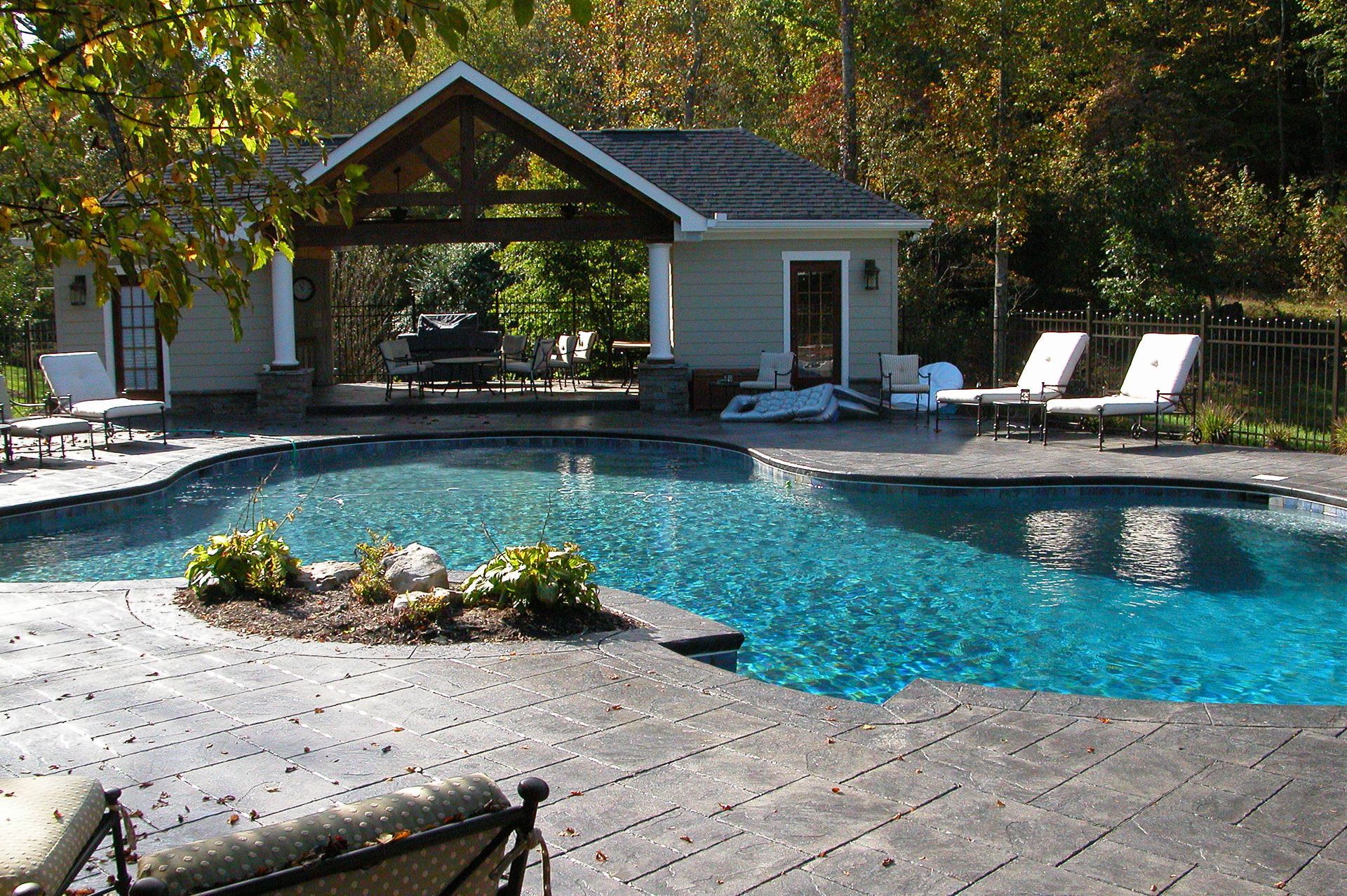 Backyard swimming pool with blue water, lounge chairs, and a shaded cabana in the trees