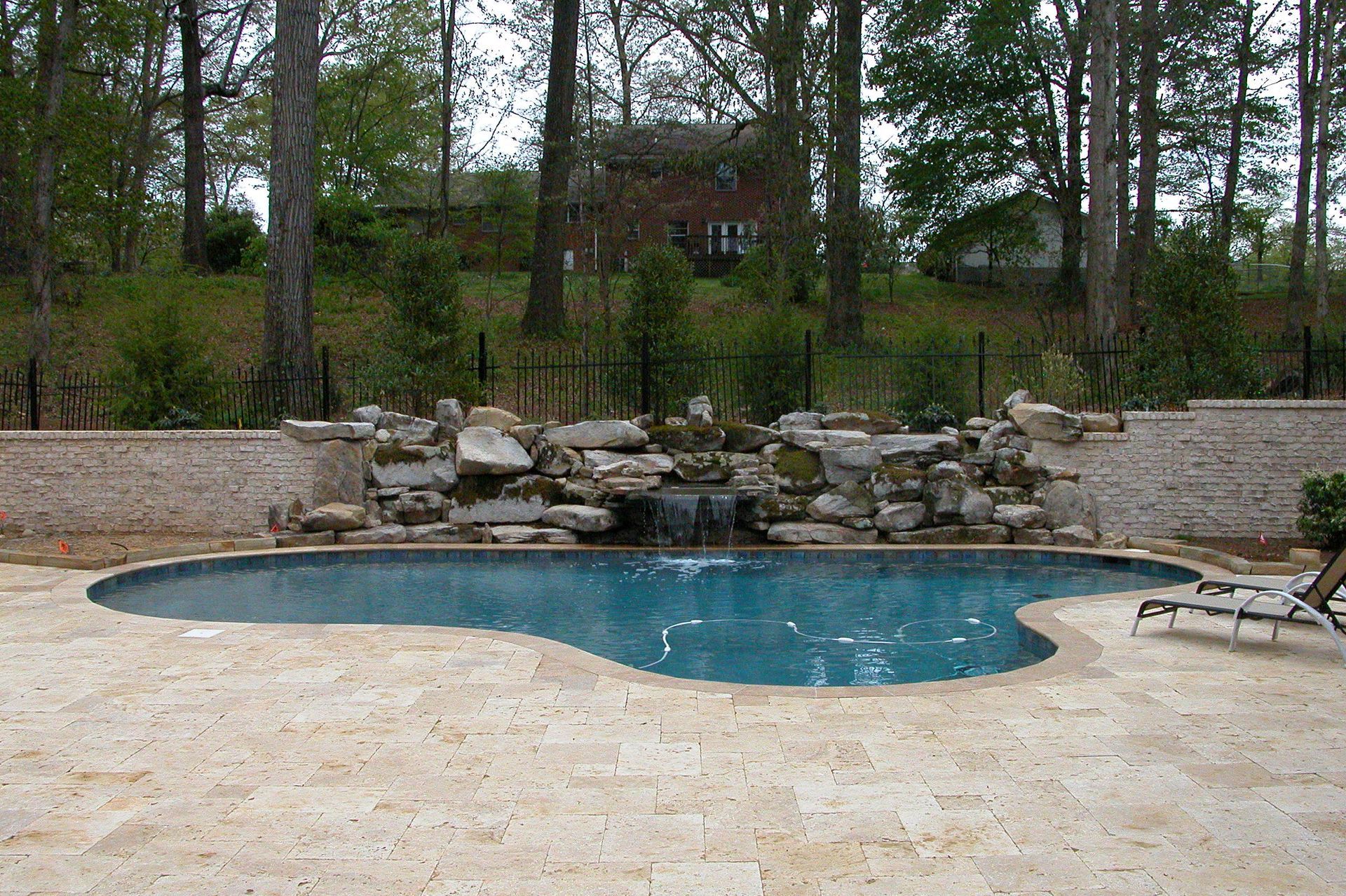 Backyard pool with rock waterfall, surrounded by stone patio and trees