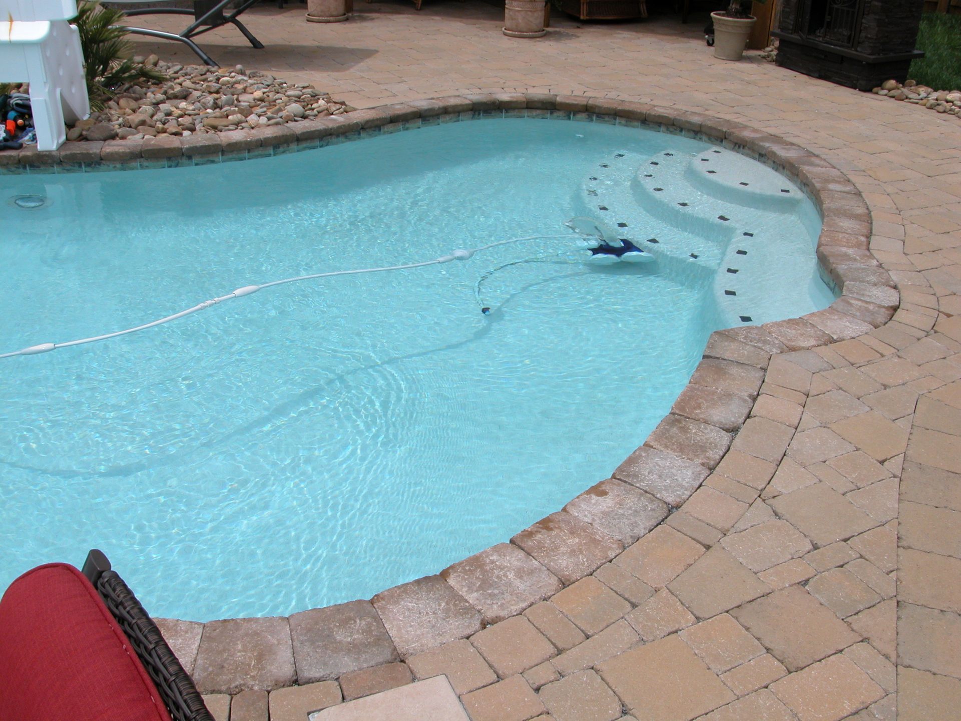 Curved backyard swimming pool with turquoise water and tan stone deck