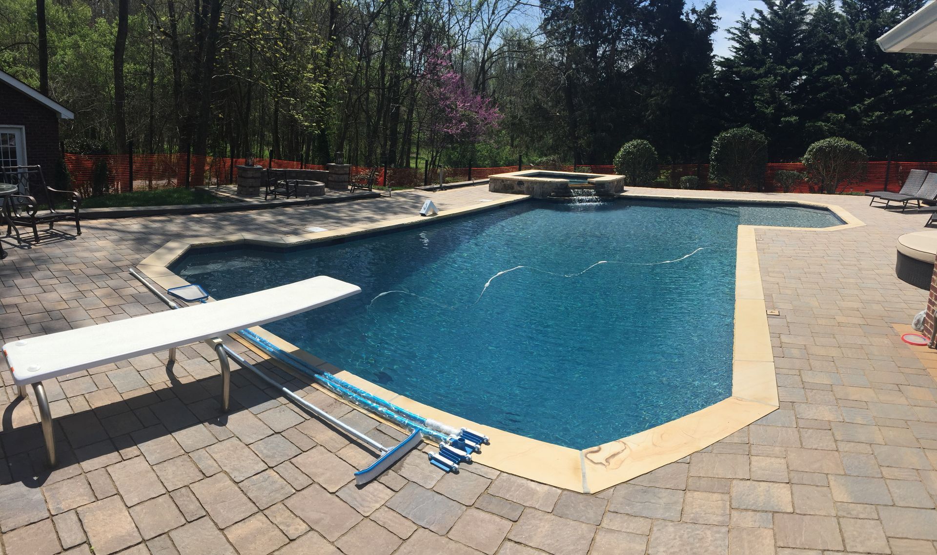 Backyard swimming pool with blue water, beige pavers, and a lounge chair on the left