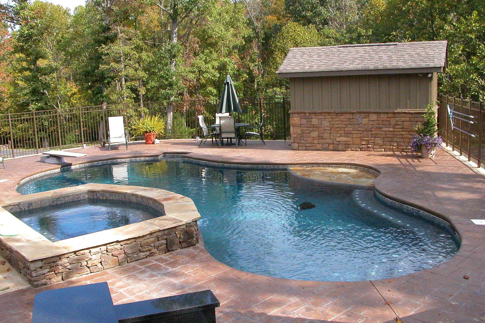 Backyard swimming pool with a hot tub, patio, and small shed surrounded by trees