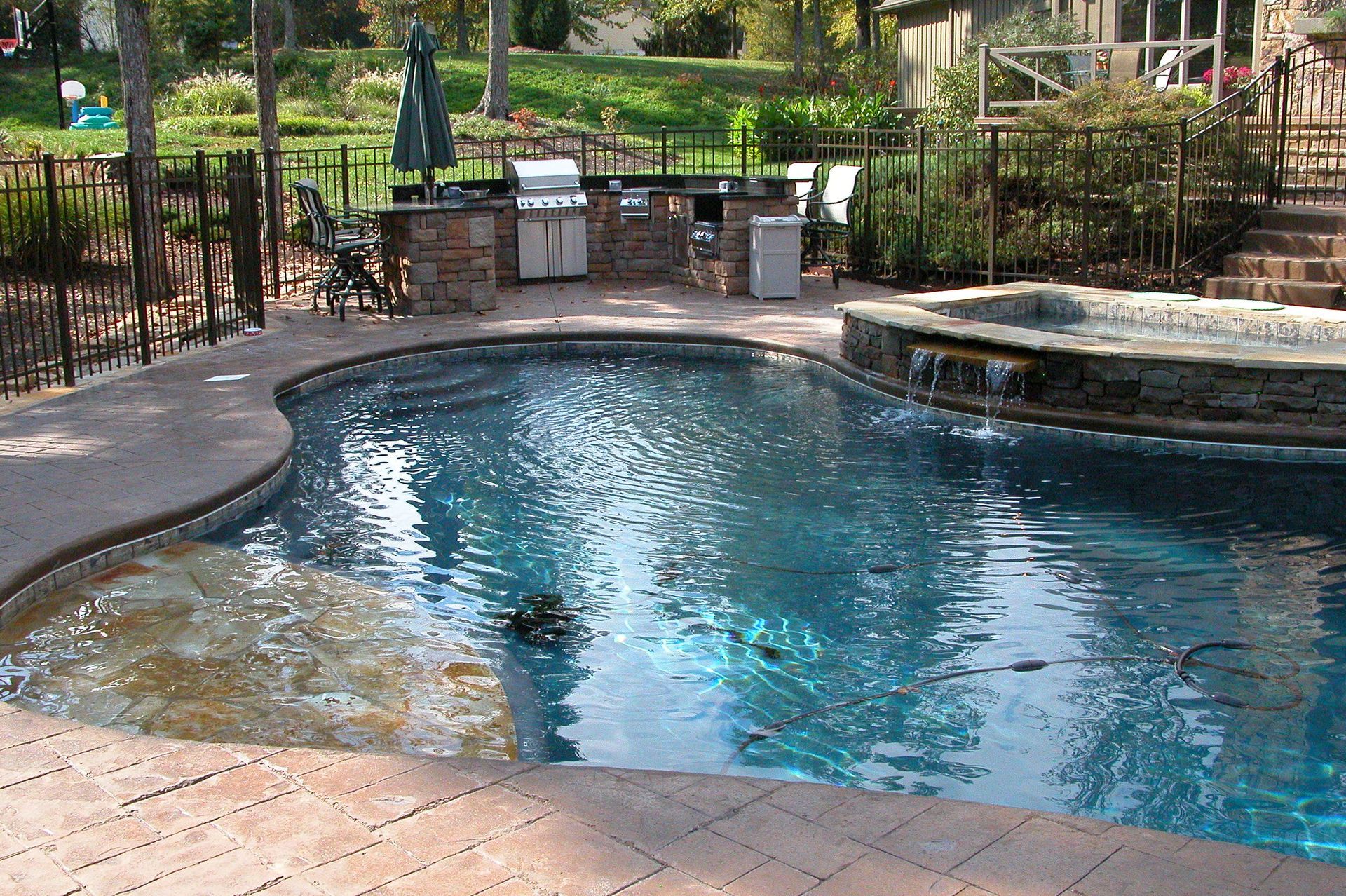 Outdoor backyard pool with blue water, stone deck, and patio seating surrounded by greenery