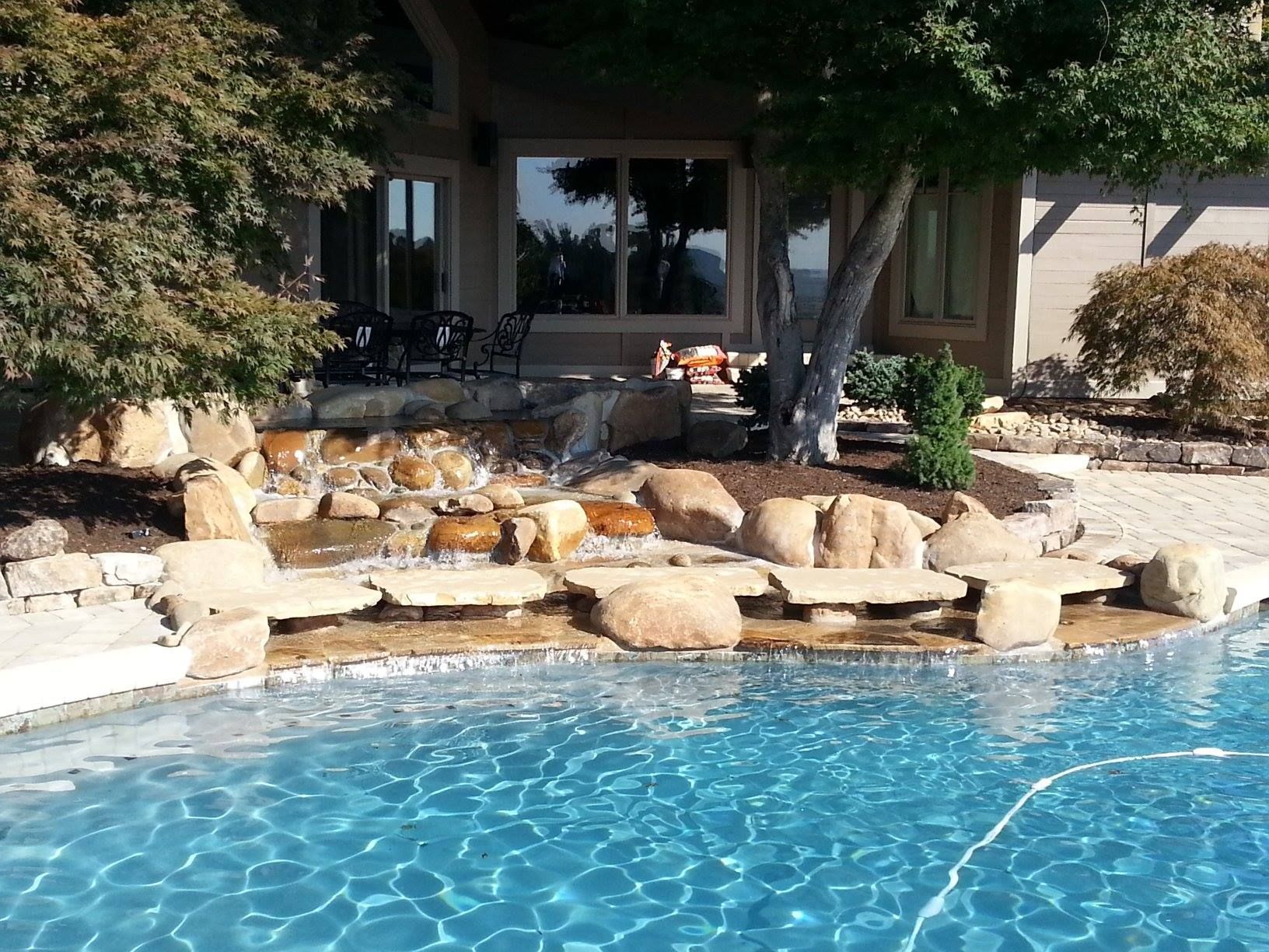 Backyard pool with rock waterfall, stone patio, and shaded patio seating.
