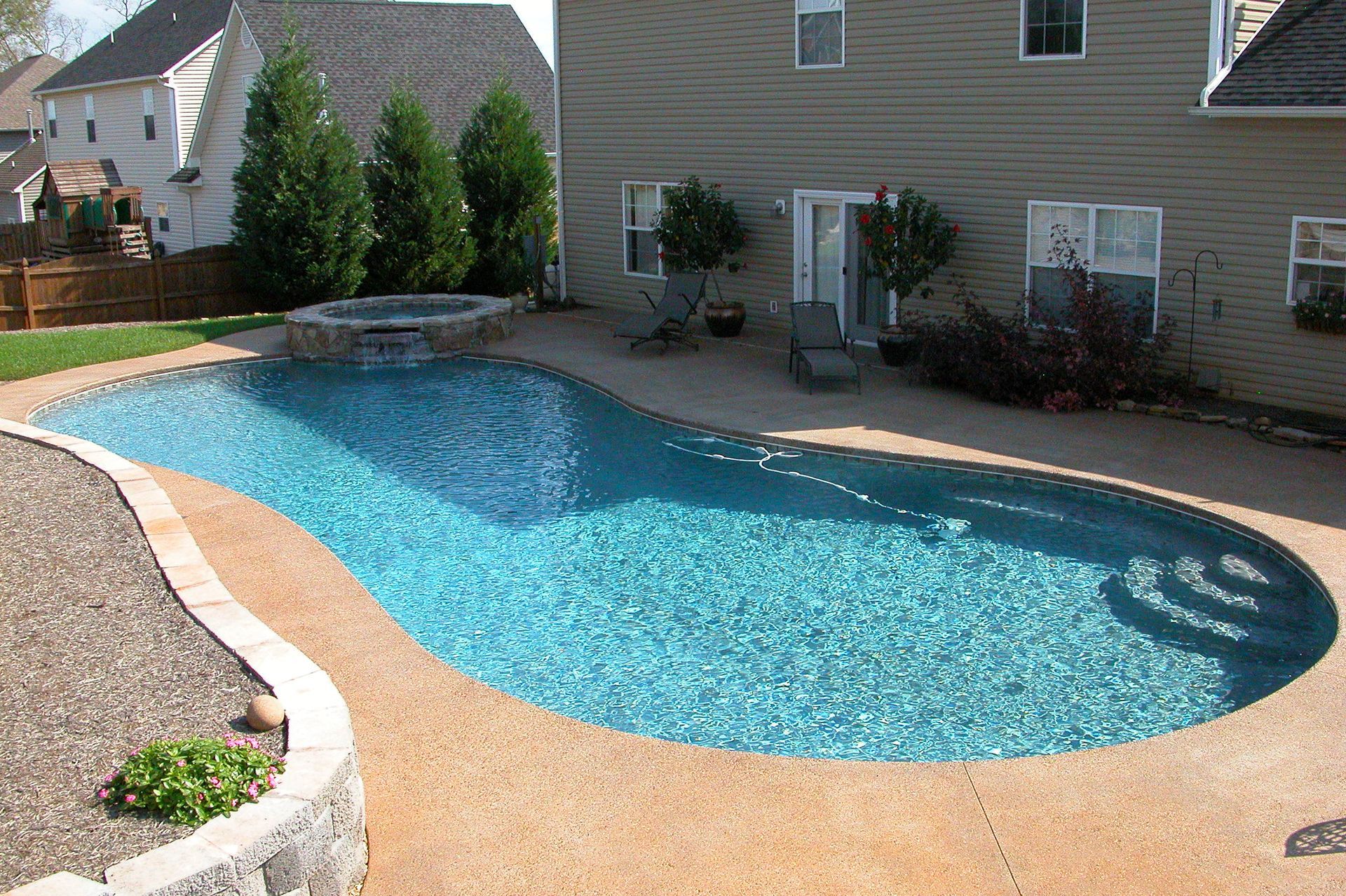 Backyard swimming pool with blue water beside a brick house and stone patio