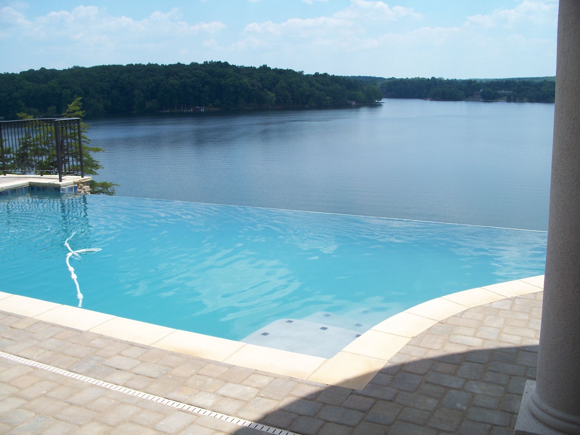 Infinity pool overlooking a calm lake under a bright blue sky