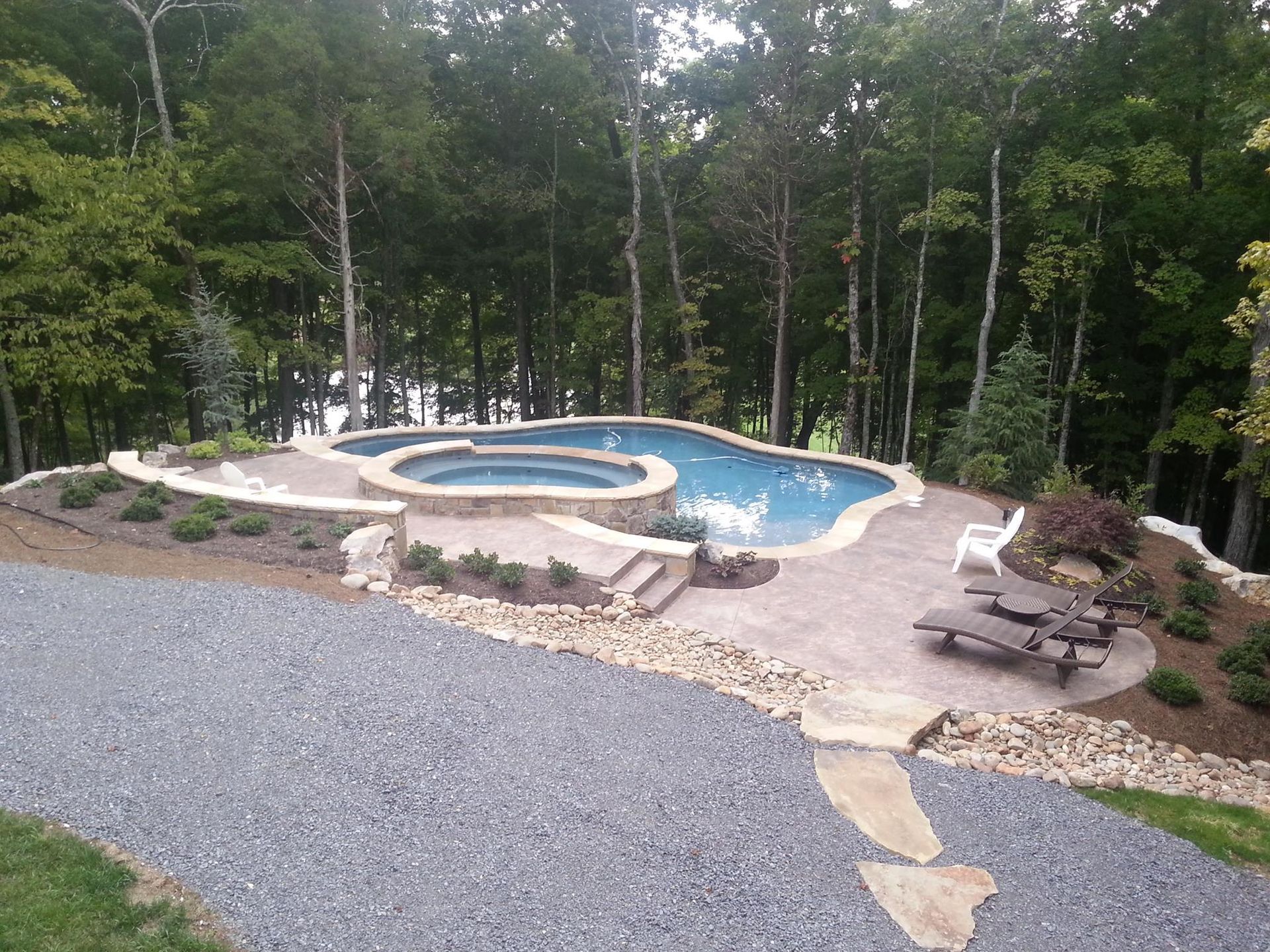 Outdoor pool with blue water, stone deck, and picnic tables surrounded by trees
