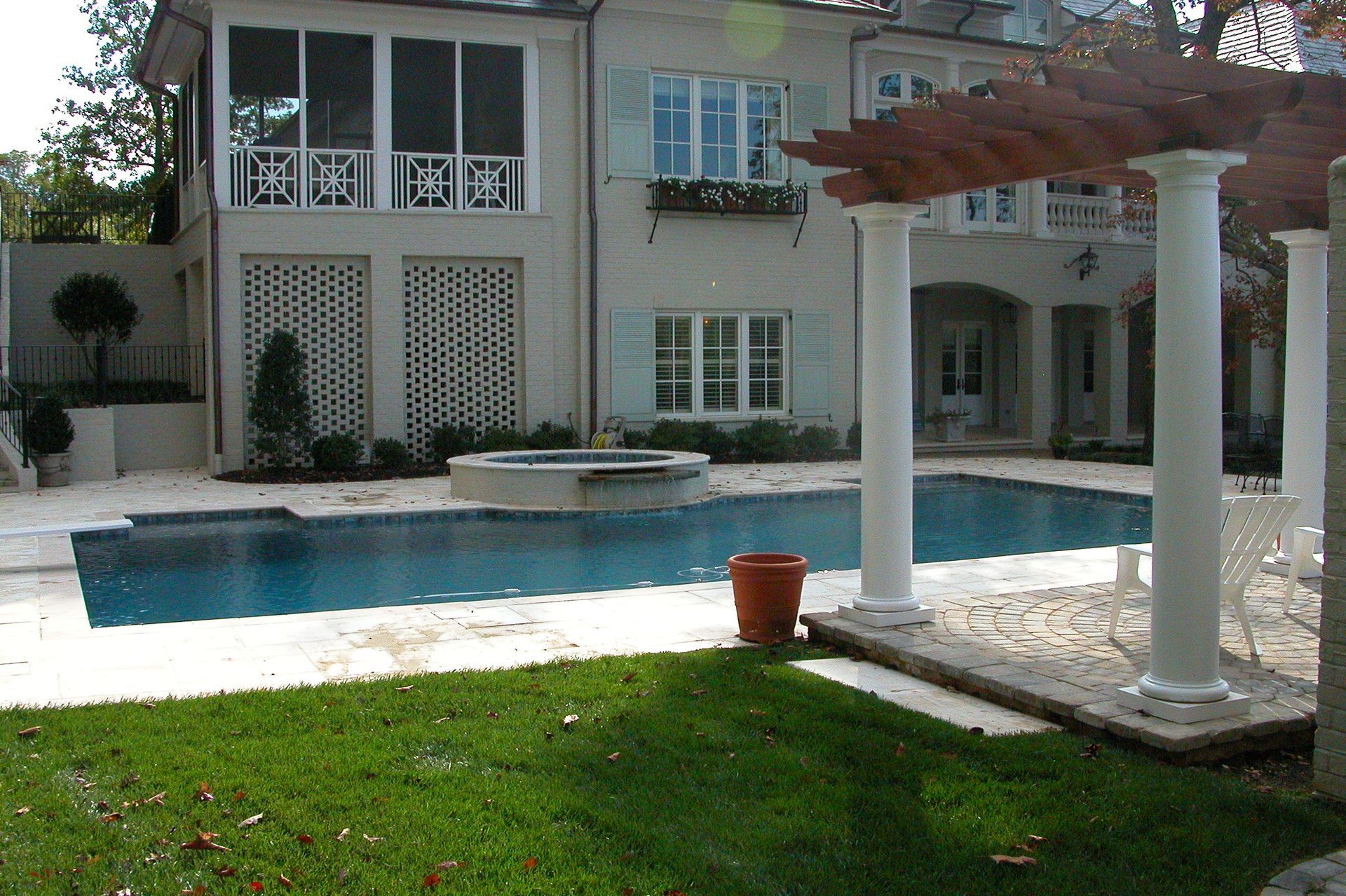 Backyard pool beside a white house with patio columns and green lawn