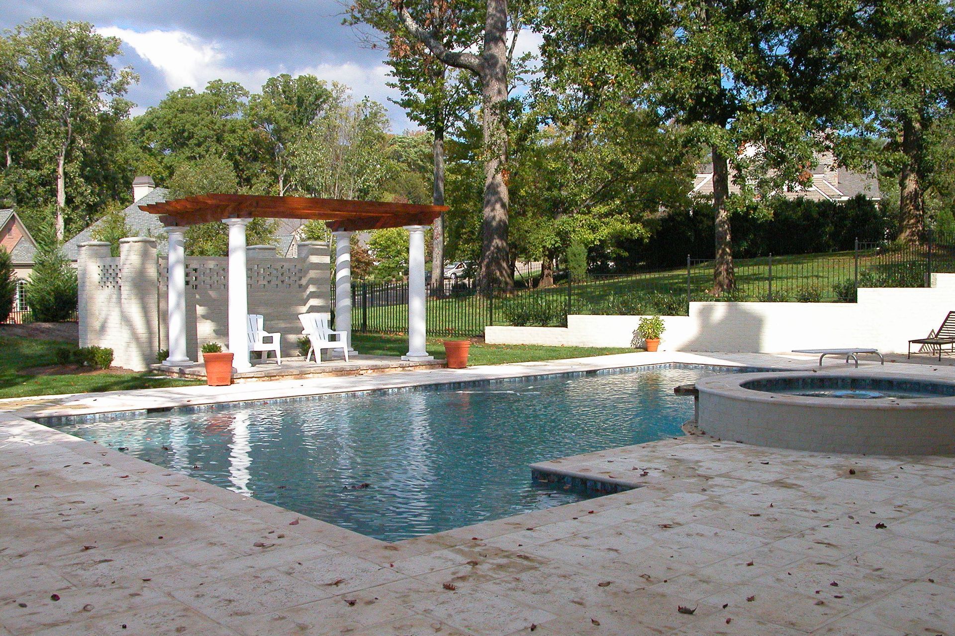 Backyard pool with stone deck, hot tub, pergola, and trees in a landscaped garden