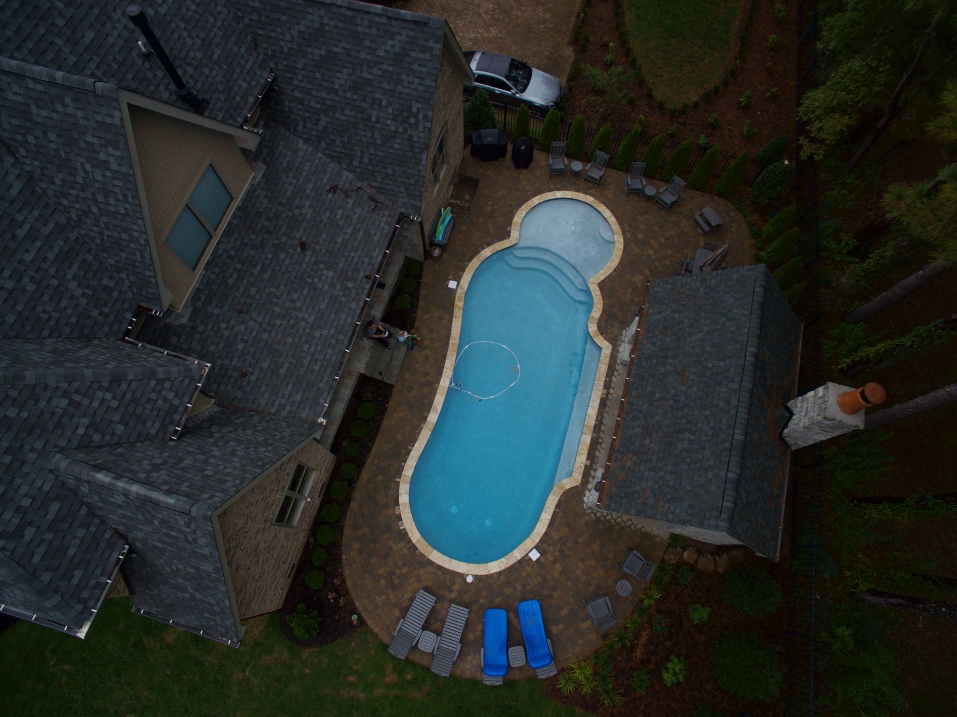 Aerial view of a backyard with a blue swimming pool beside a house and patio furniture.