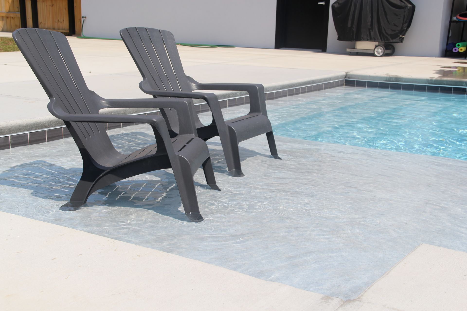 Two dark gray lounge chairs beside a swimming pool with blue water and a light concrete deck