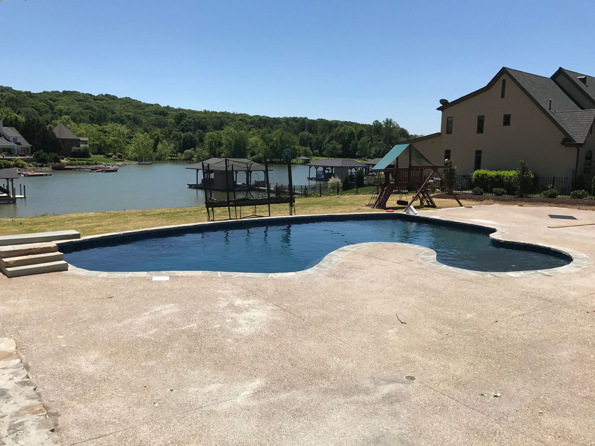 Backyard pool with lake view, dock, and houses on a sunny day