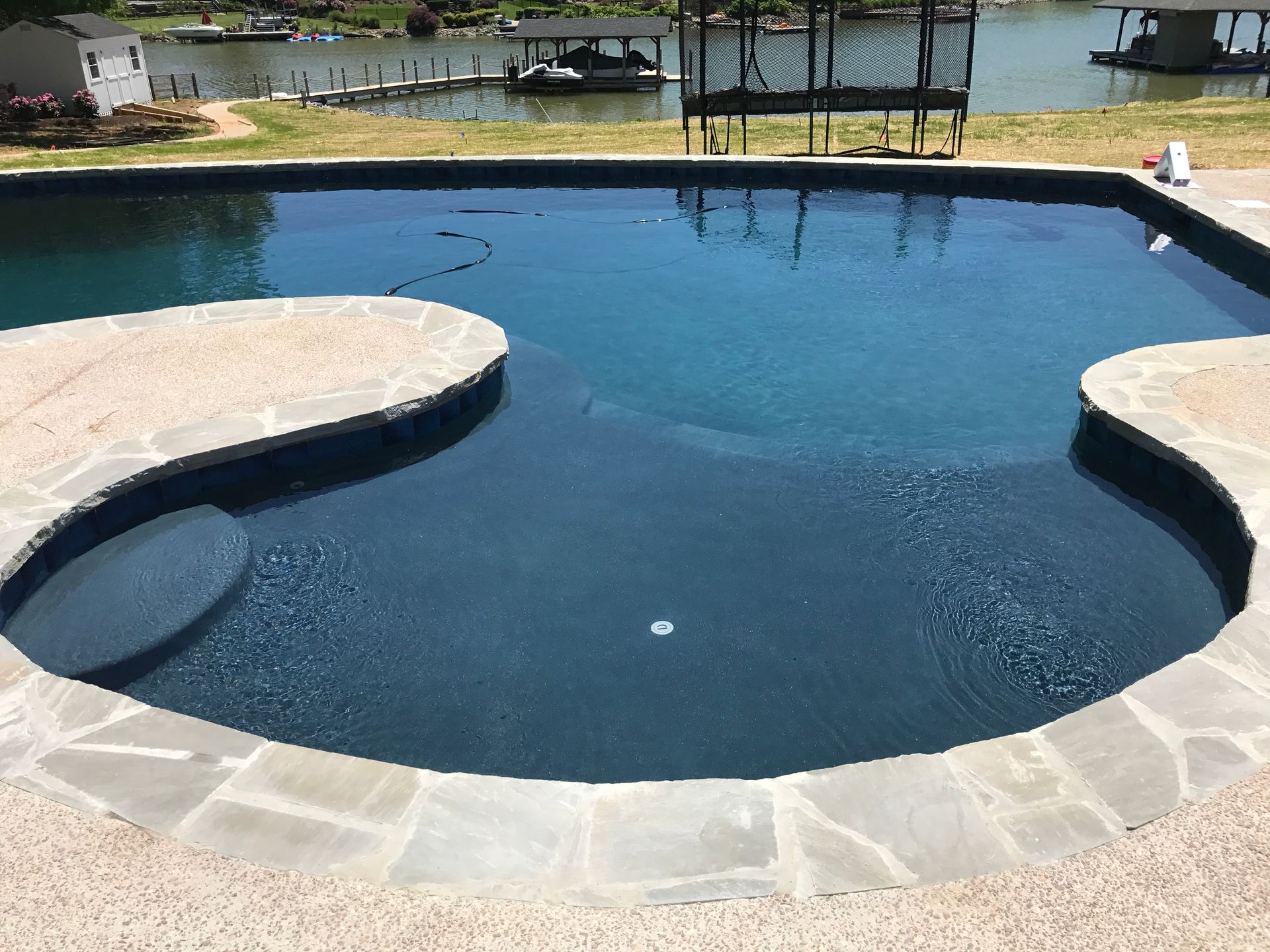 Backyard swimming pool with dark blue water, curved stone edges, and a patio overlooking the lake.