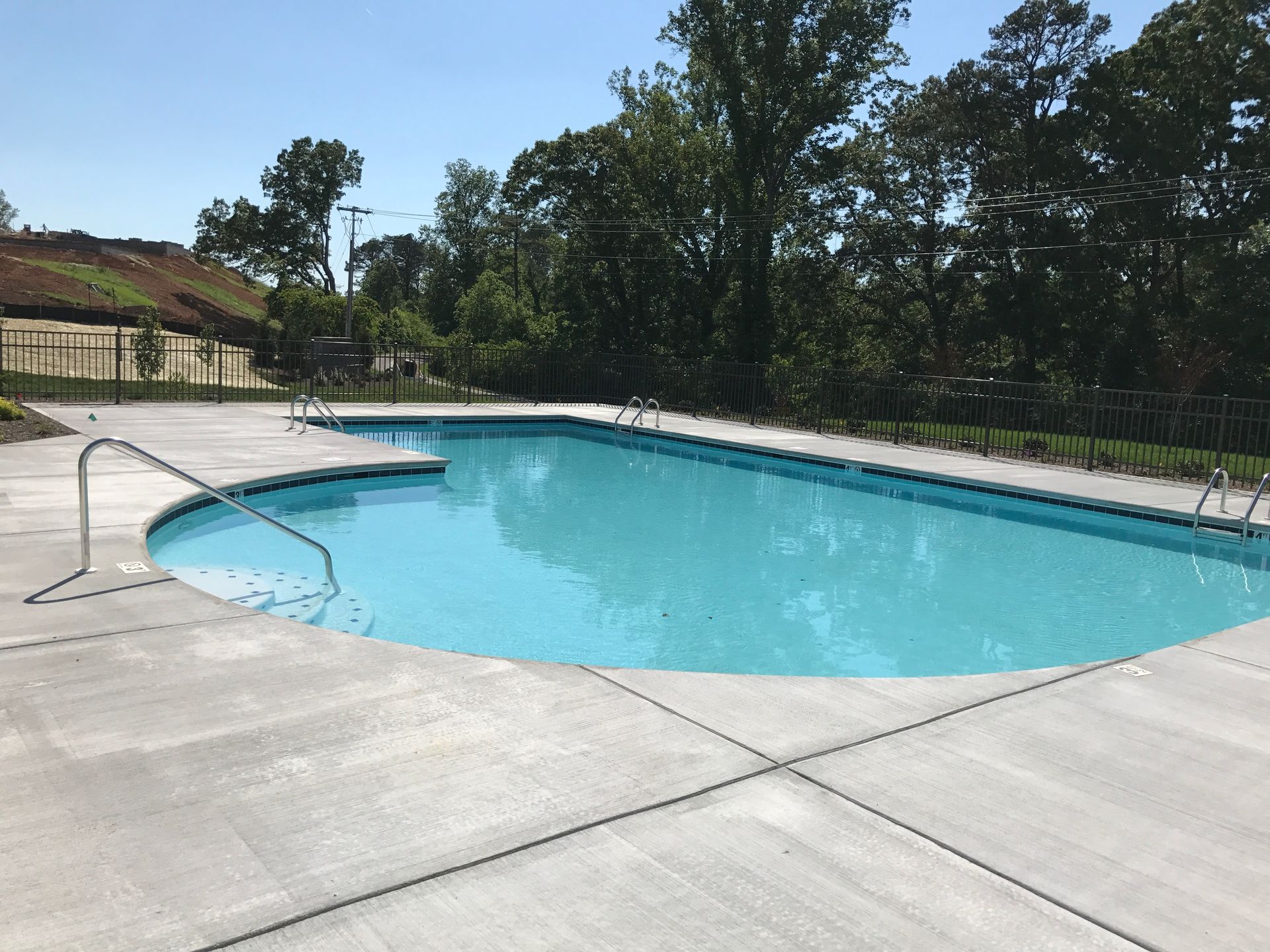 Outdoor swimming pool with clear blue water, concrete deck, and trees in the background
