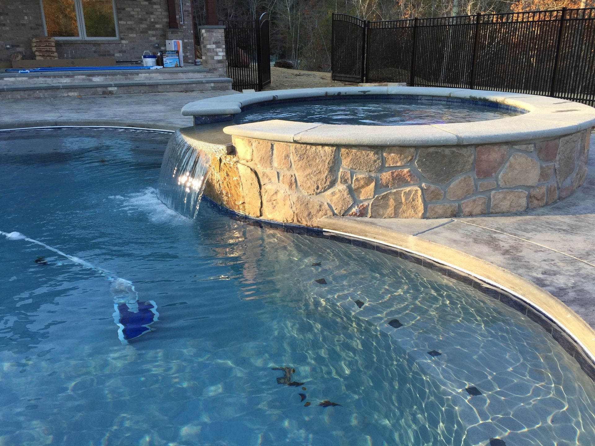 Stone hot tub spilling into a blue swimming pool at a resort-style patio