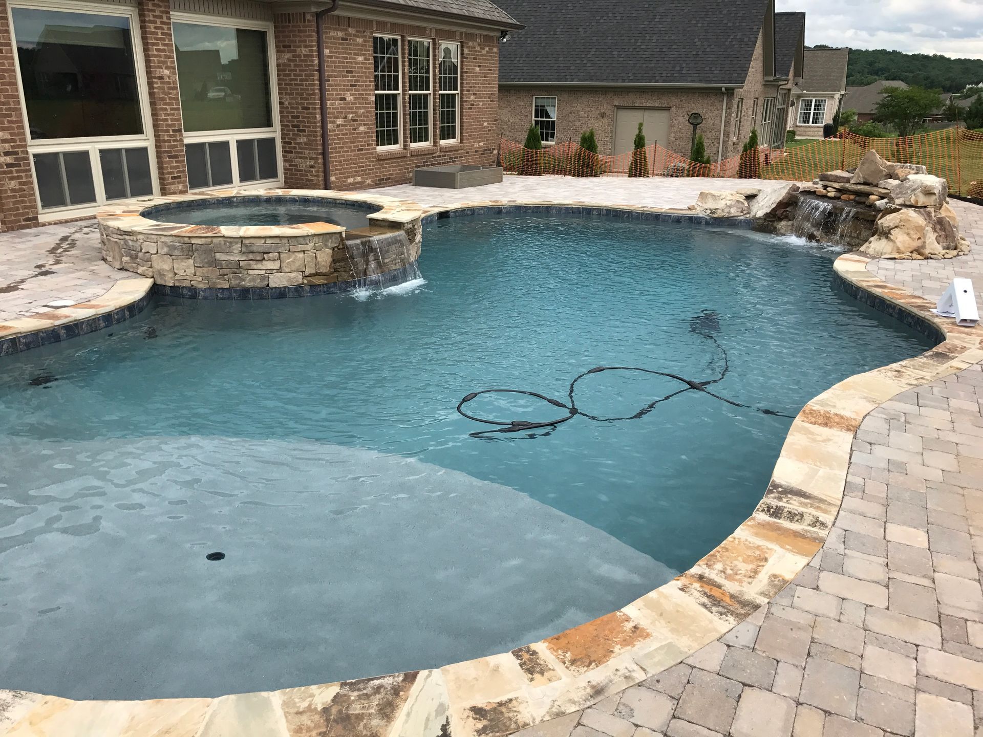 Backyard swimming pool with blue water, stone coping, and a built-in spa beside a brick house