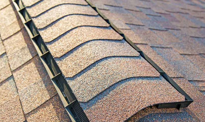 A close up of a roof with shingles and a drain on it.