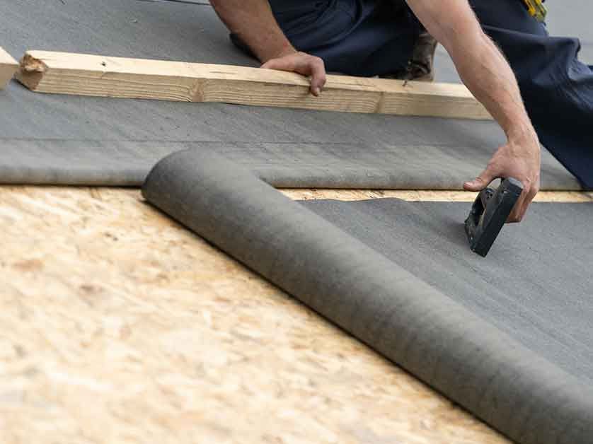 A man is laying a roll of fabric on a roof.