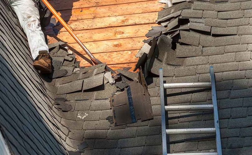 A man is working on a roof with a shovel and ladder.