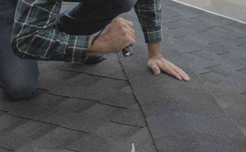 A man is kneeling down on a roof with a hammer.
