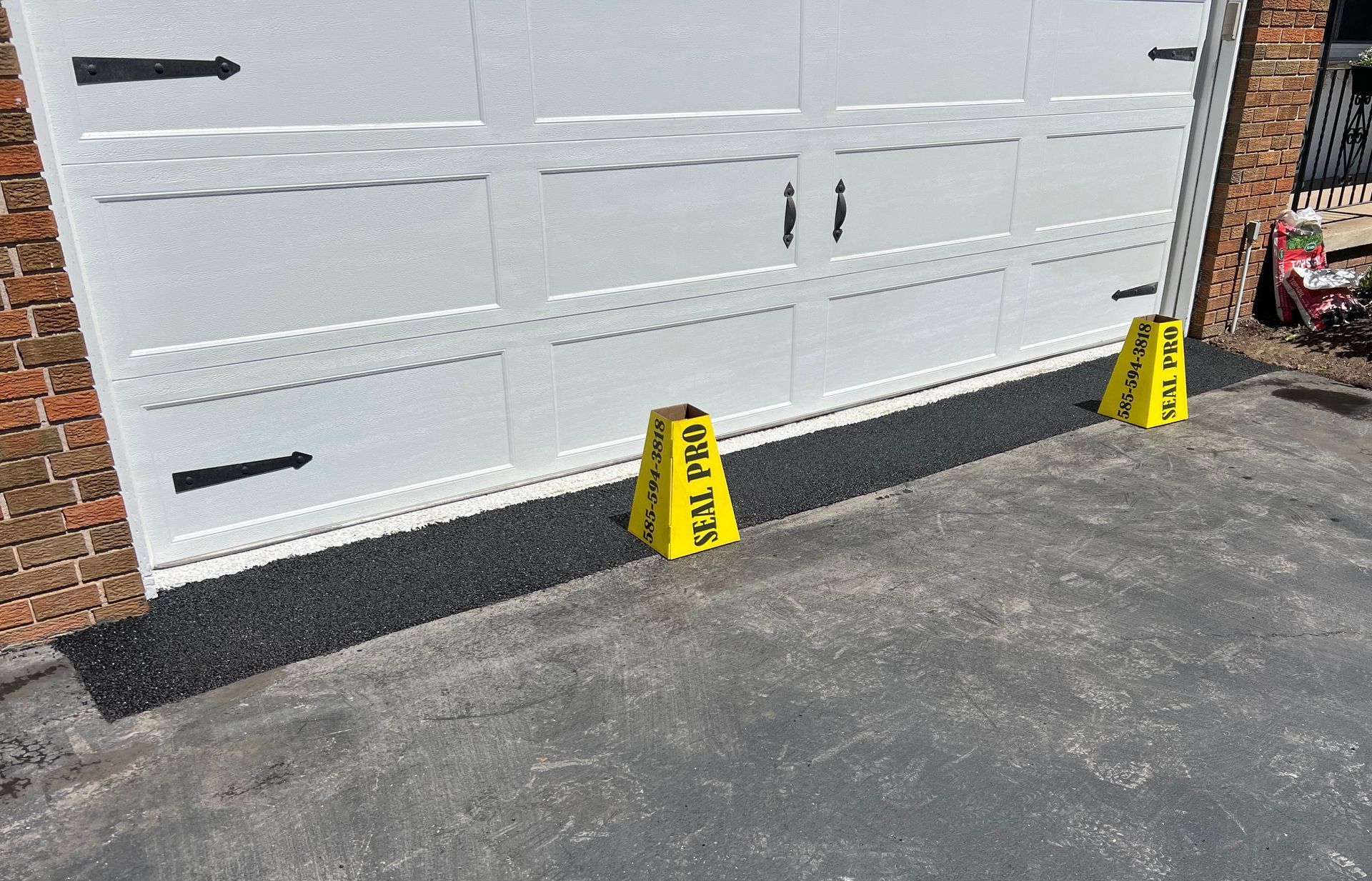 A white garage door with repaired asphalt in front of it.