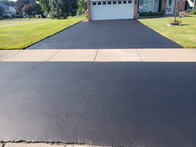 a black driveway with a white garage door is in front of a house