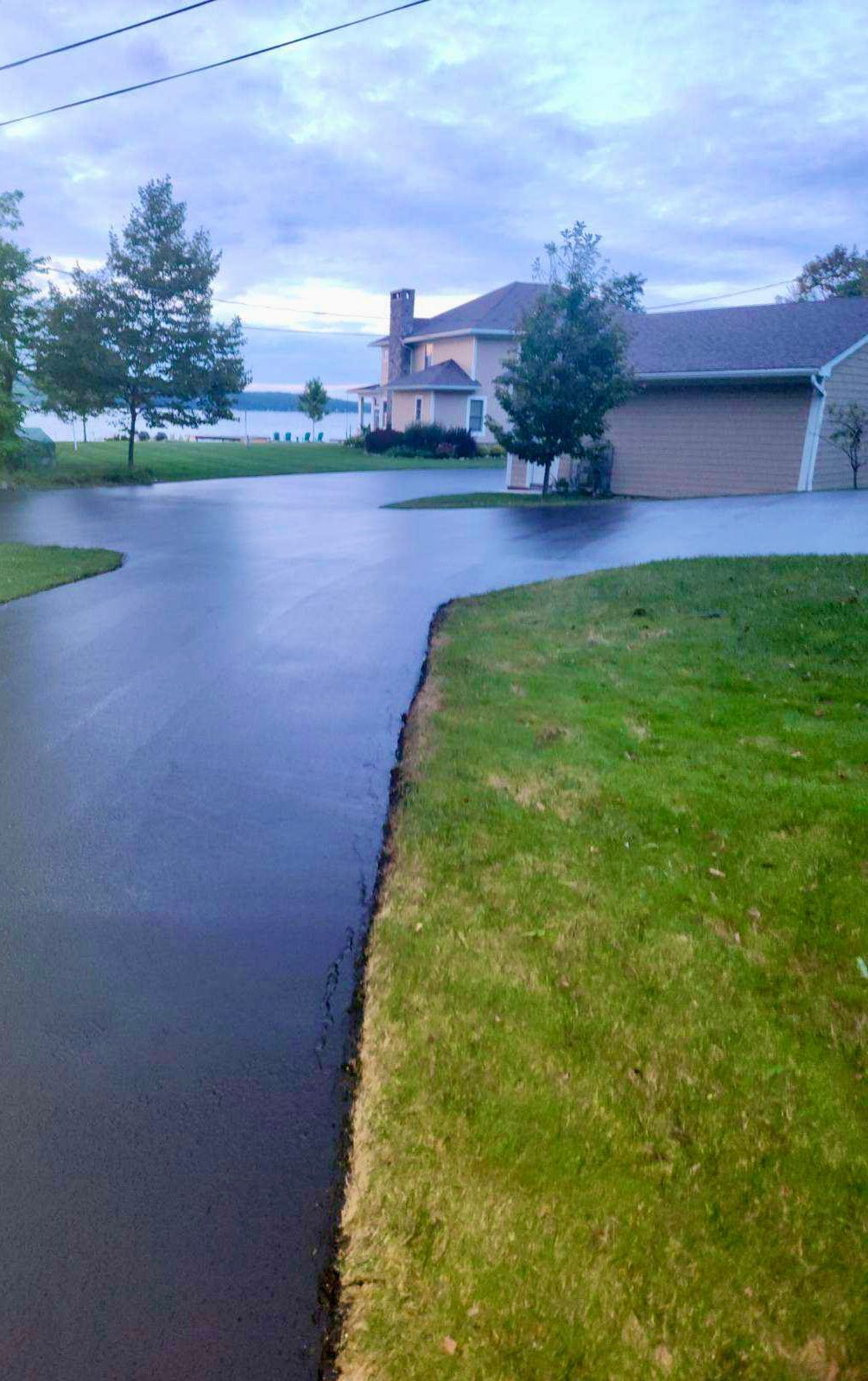 a driveway leading to a house with a lake in the background