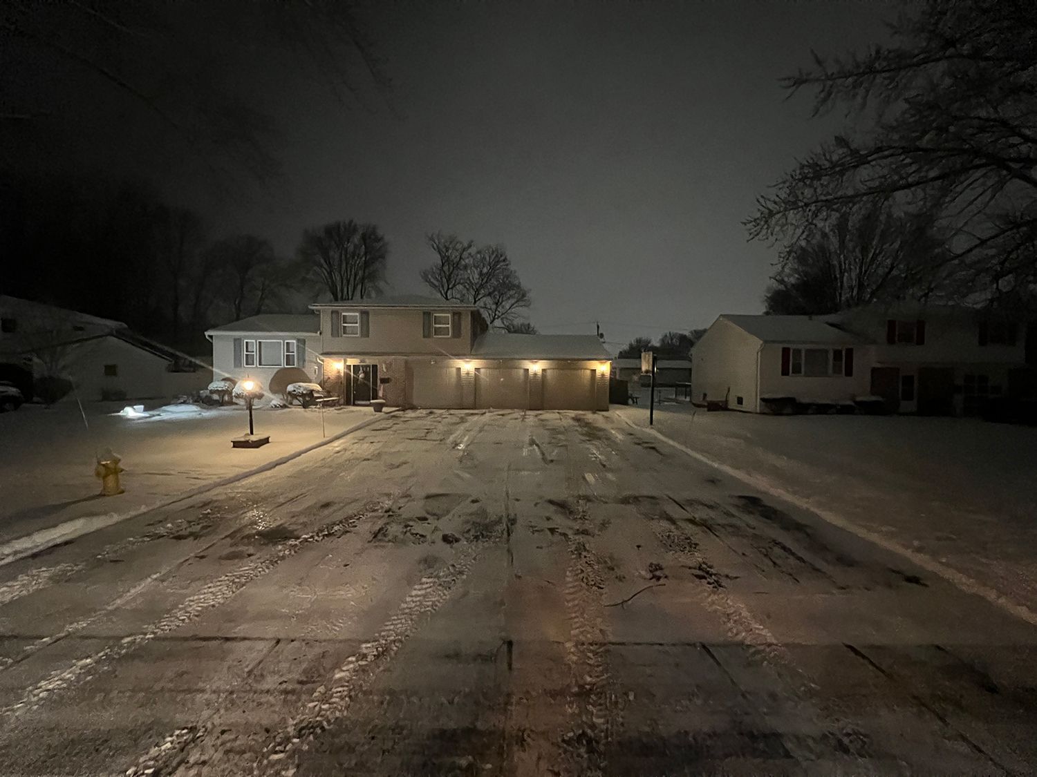 a snowy driveway with a house in the background at night