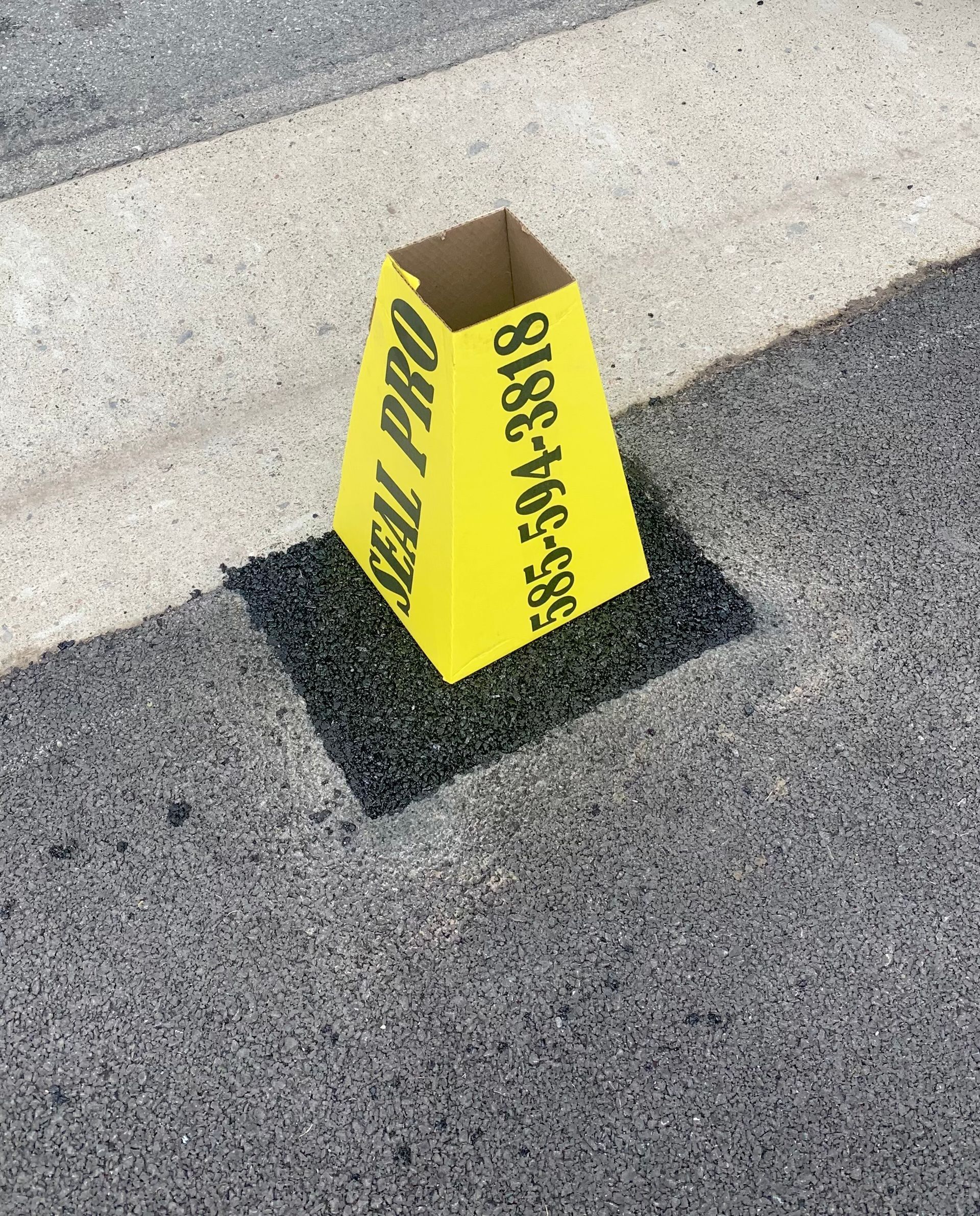 a yellow cone with a phone number on it is on the side of the road