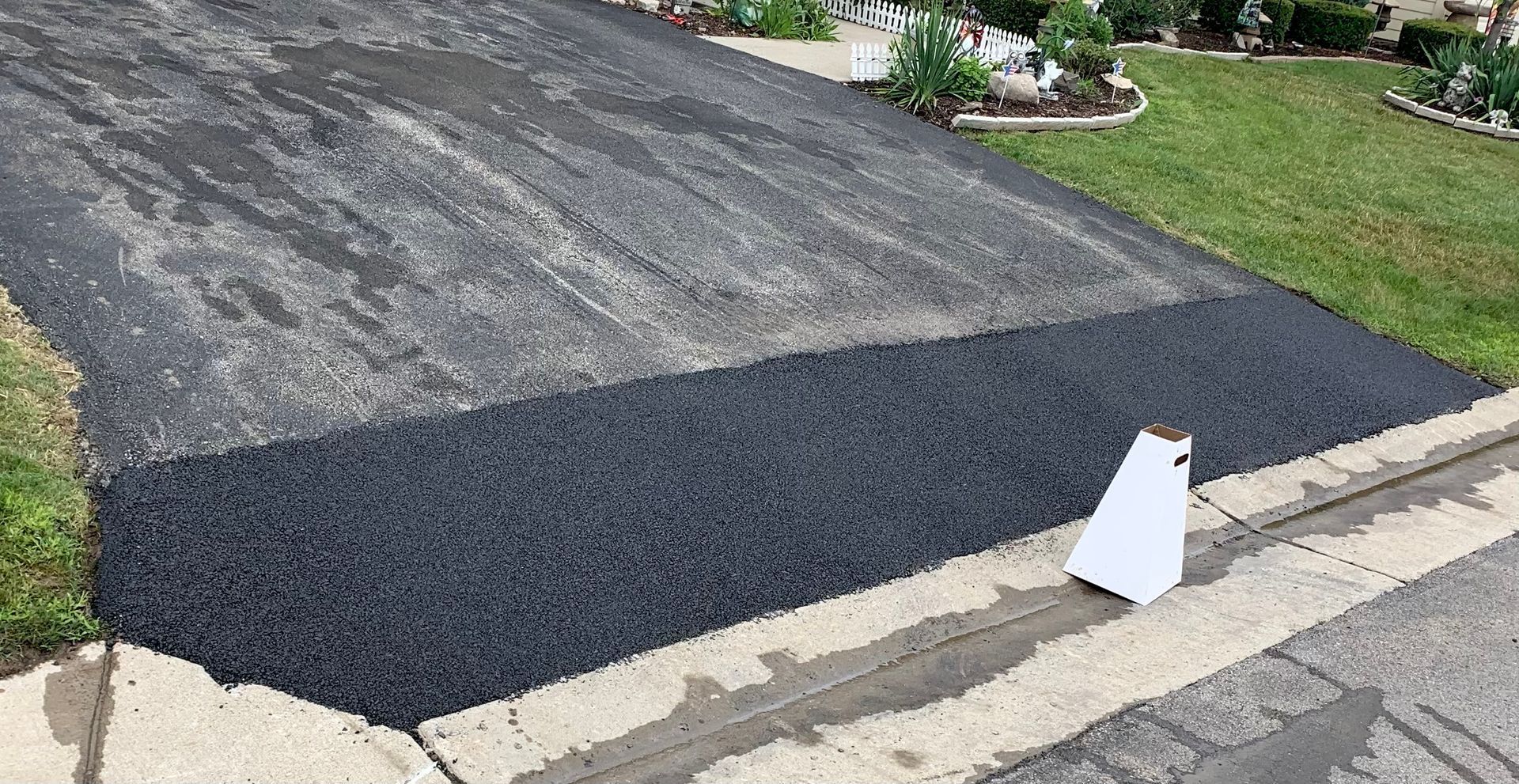 a black asphalt driveway with a white sign on the sidewalk
