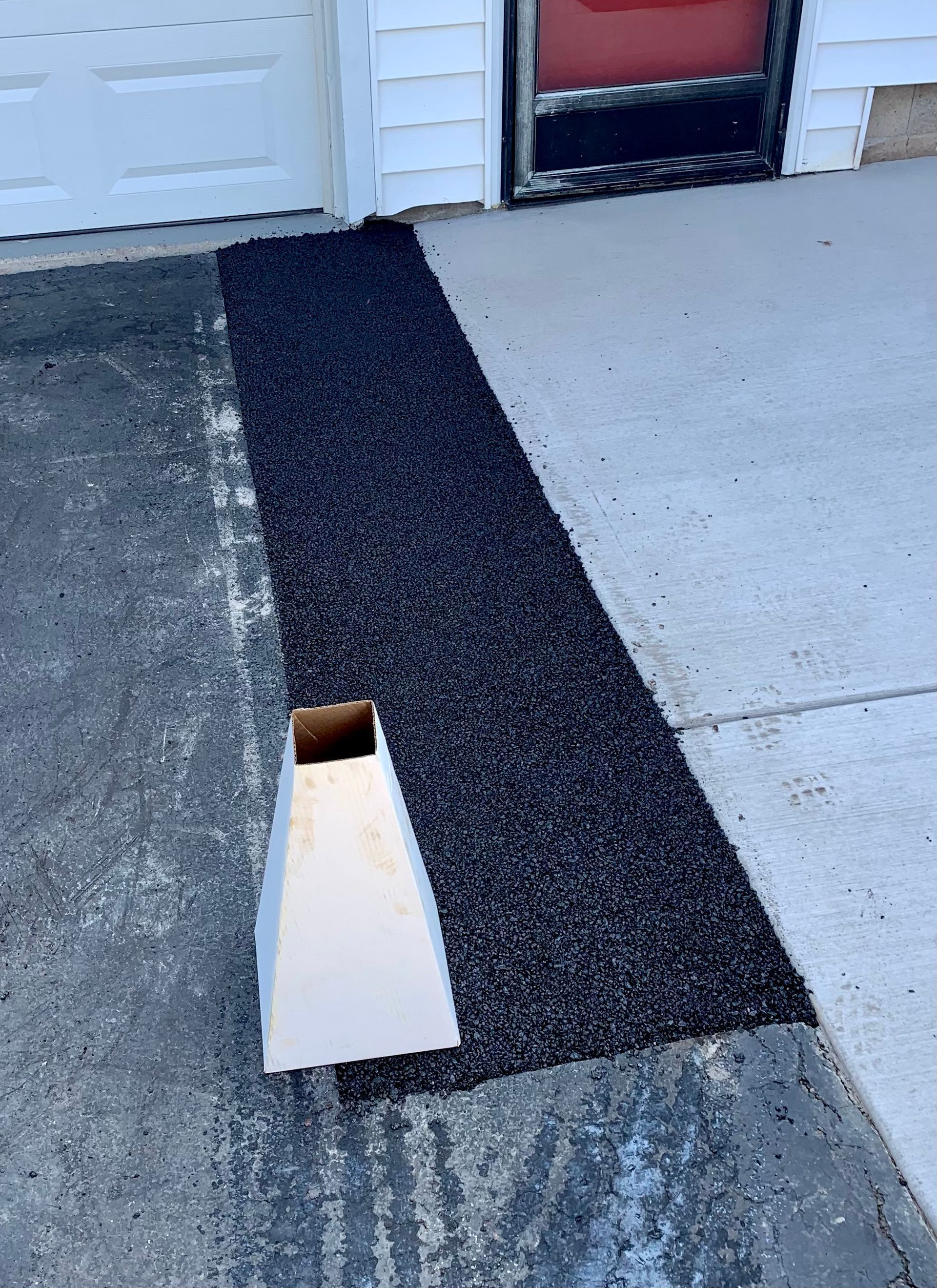 a black door mat is sitting on the sidewalk in front of a garage door