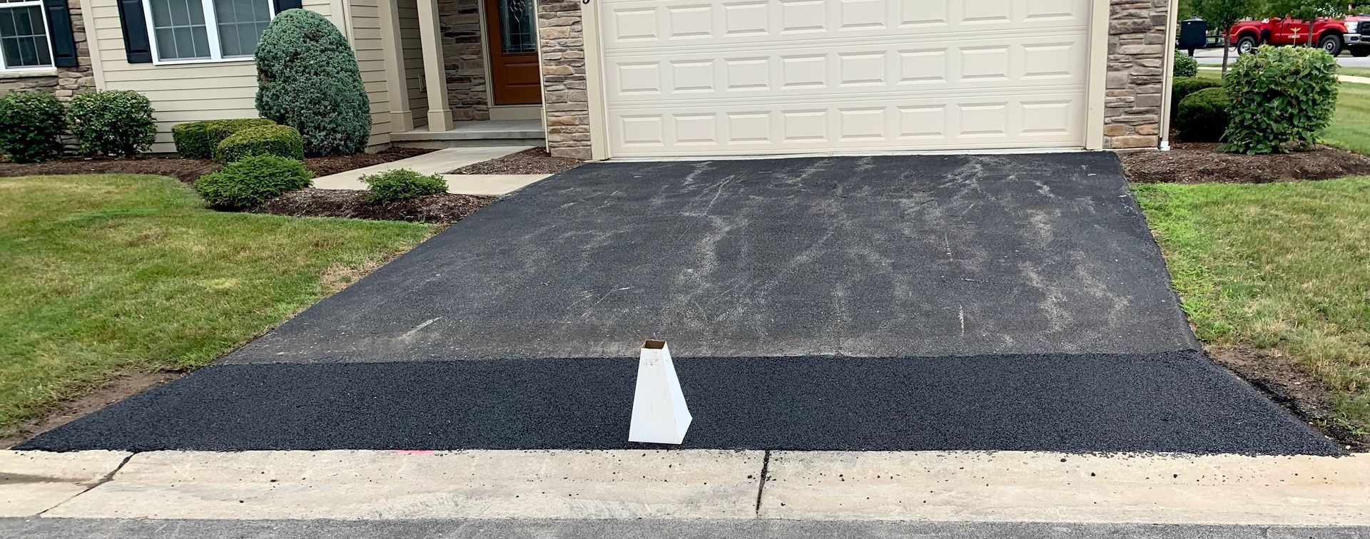a black driveway with a white line in the middle is in front of a house