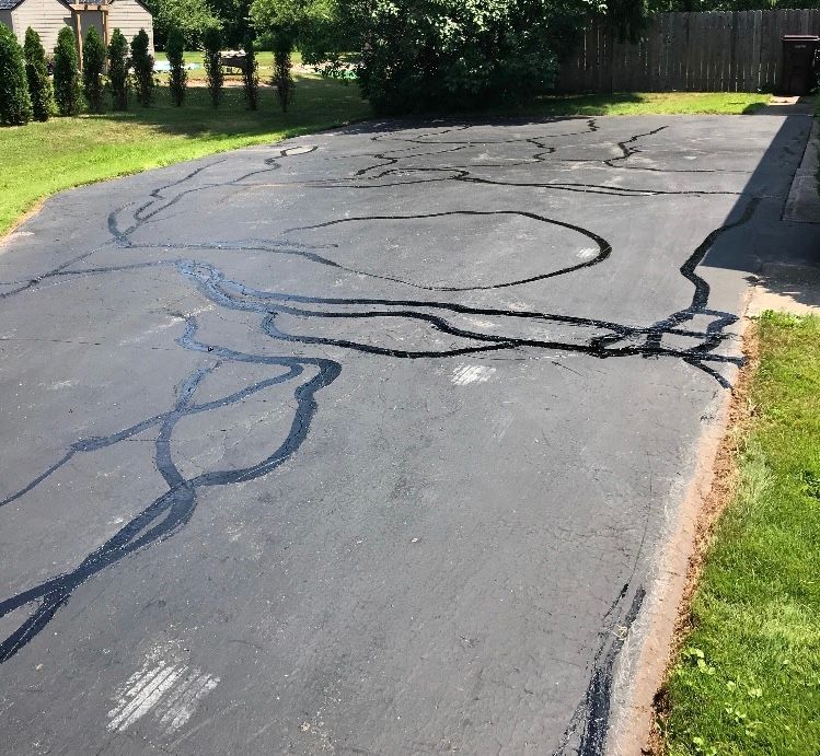 a driveway with a lot of cracks in it and a fence in the background