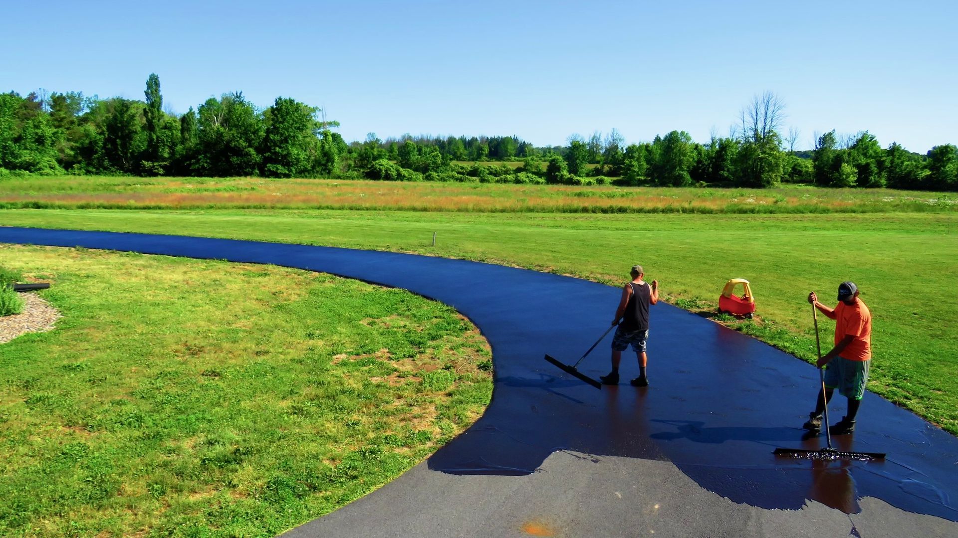 two men are painting a driveway in a grassy field