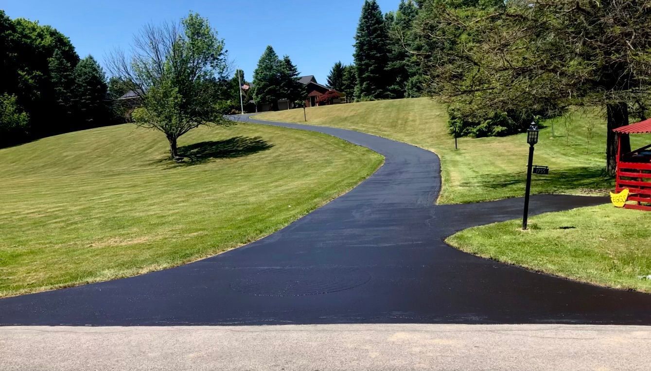 a black asphalt driveway going through a lush green field