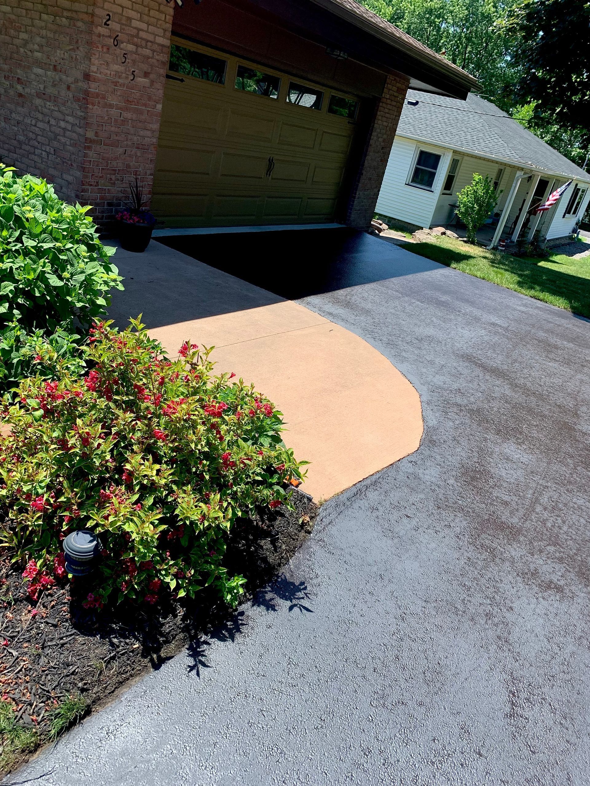 a driveway leading to a garage with flowers in the foreground and a house in the background