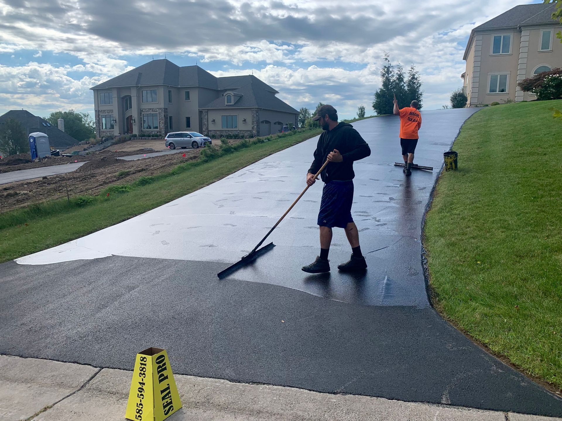 two men are painting a driveway in front of a house