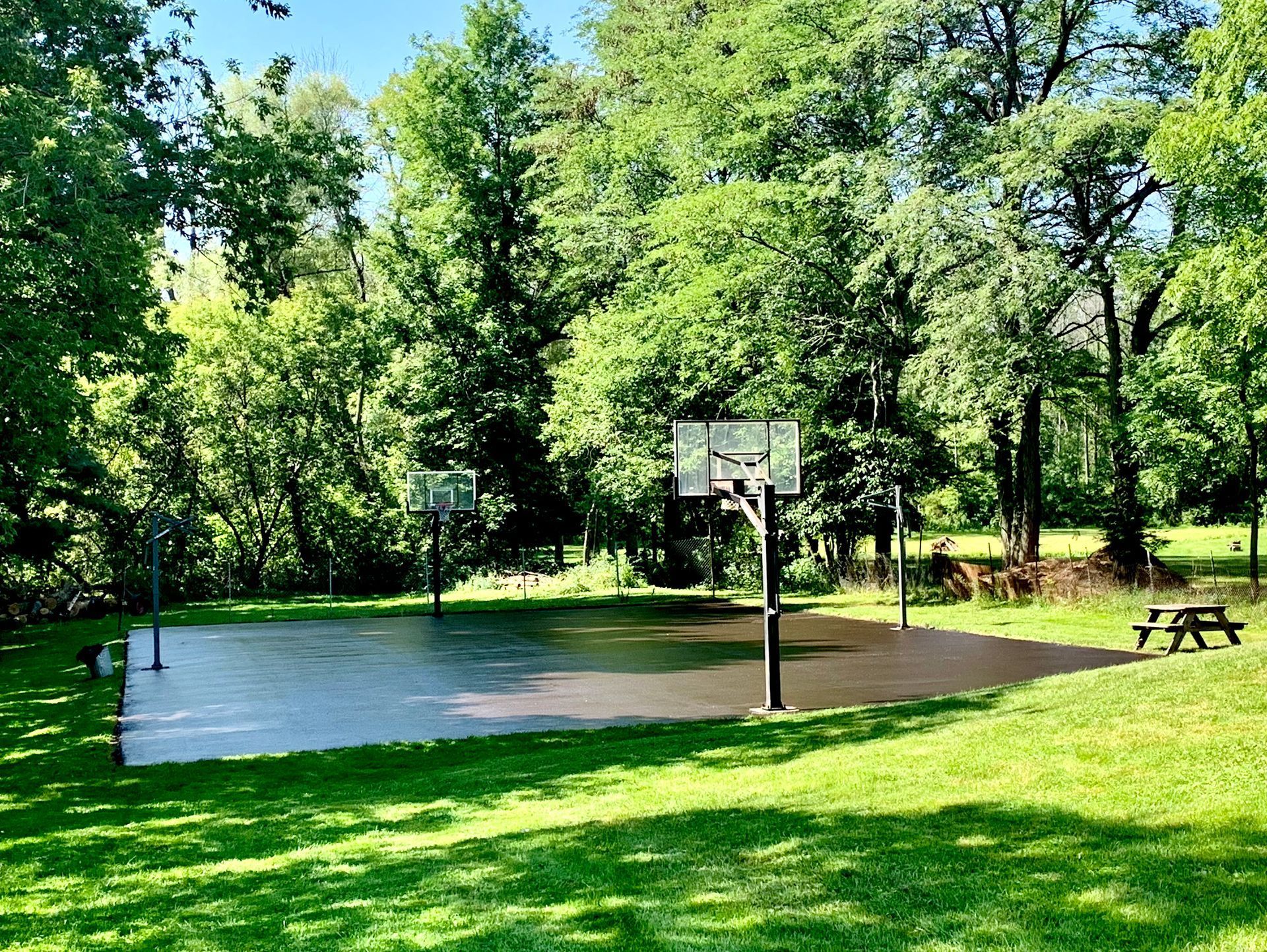 a basketball court in a park surrounded by trees and a picnic table