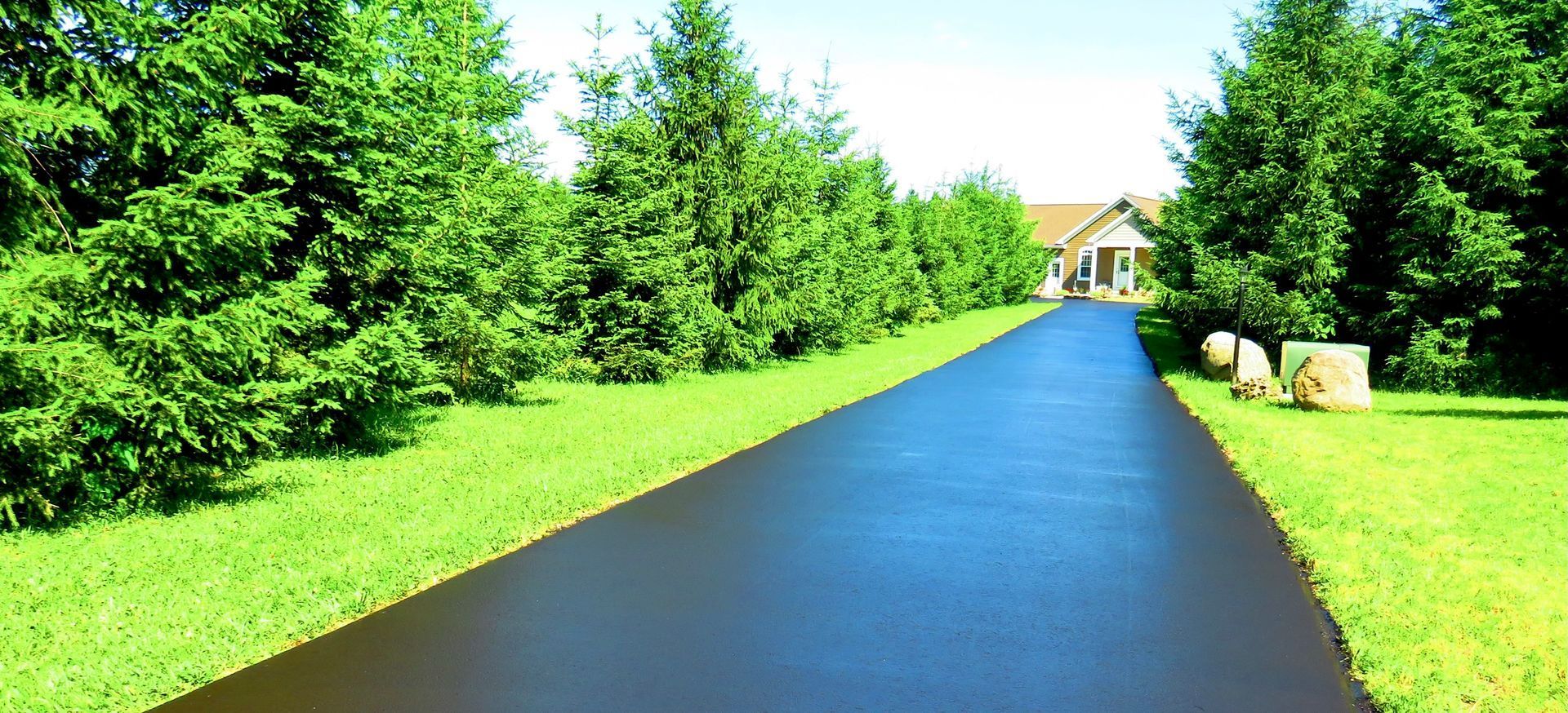 a driveway leading to a house surrounded by trees and grass