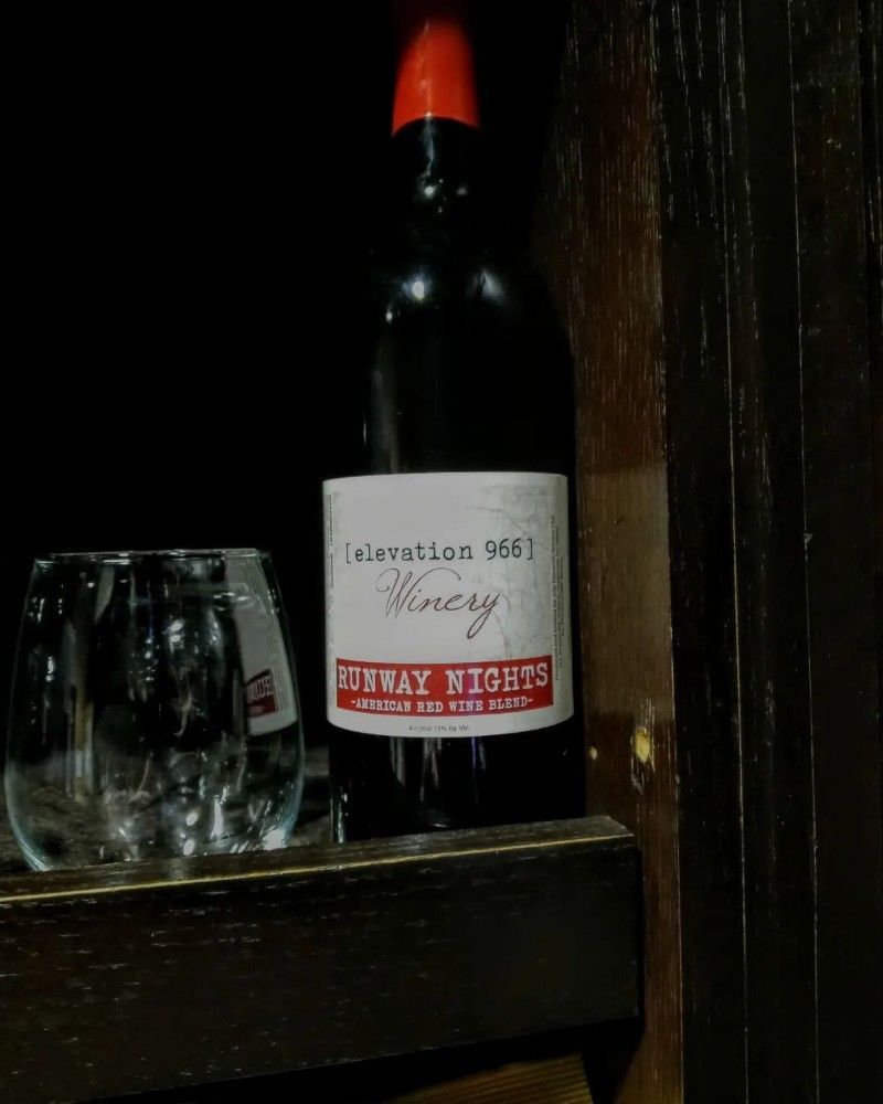 A bottle of wine is sitting on a wooden shelf next to a glass