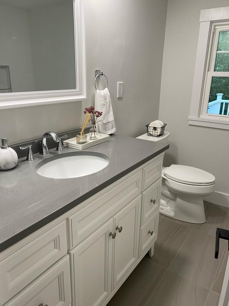 a bathroom with a sink, toilet, mirror and window
