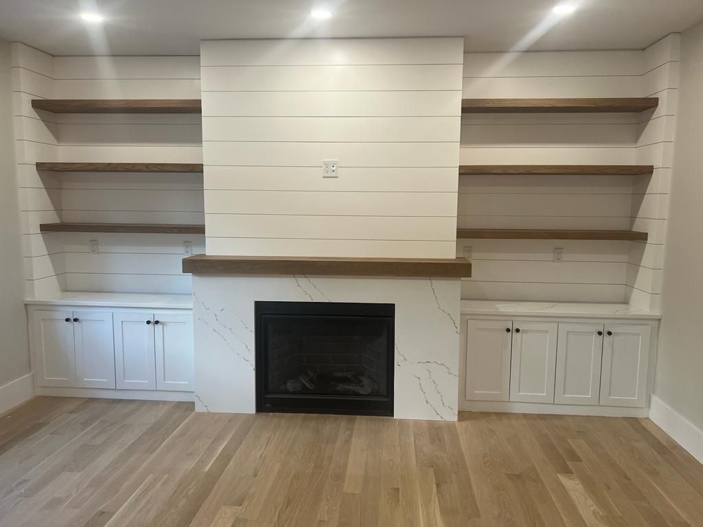 an empty living room with a fireplace and shelves