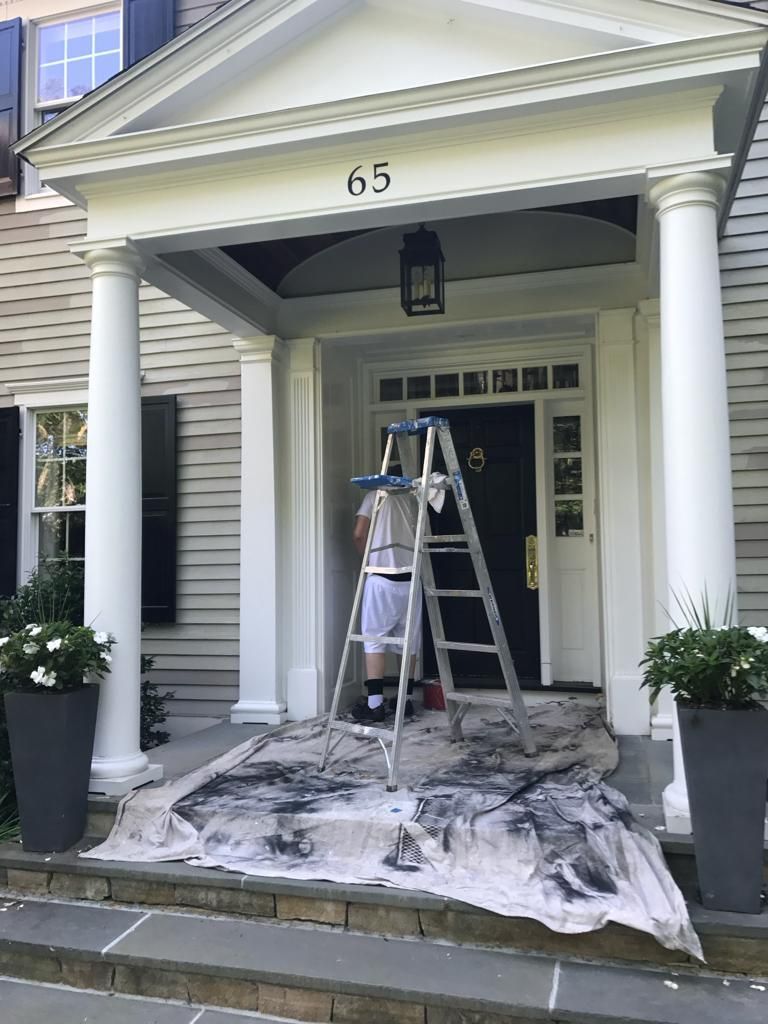 a man is standing on a ladder painting the front door of a house