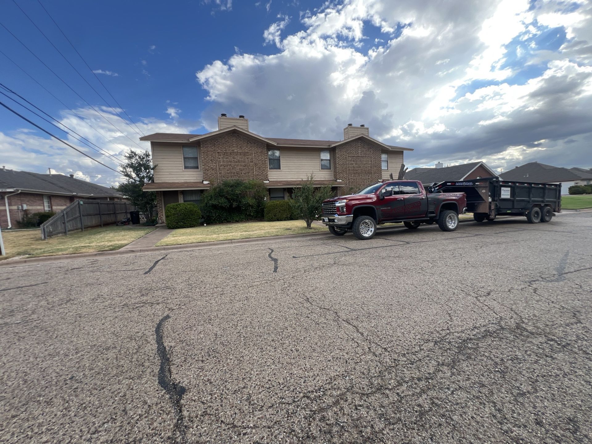 A red truck with a trailer attached to it is parked in front of a house.