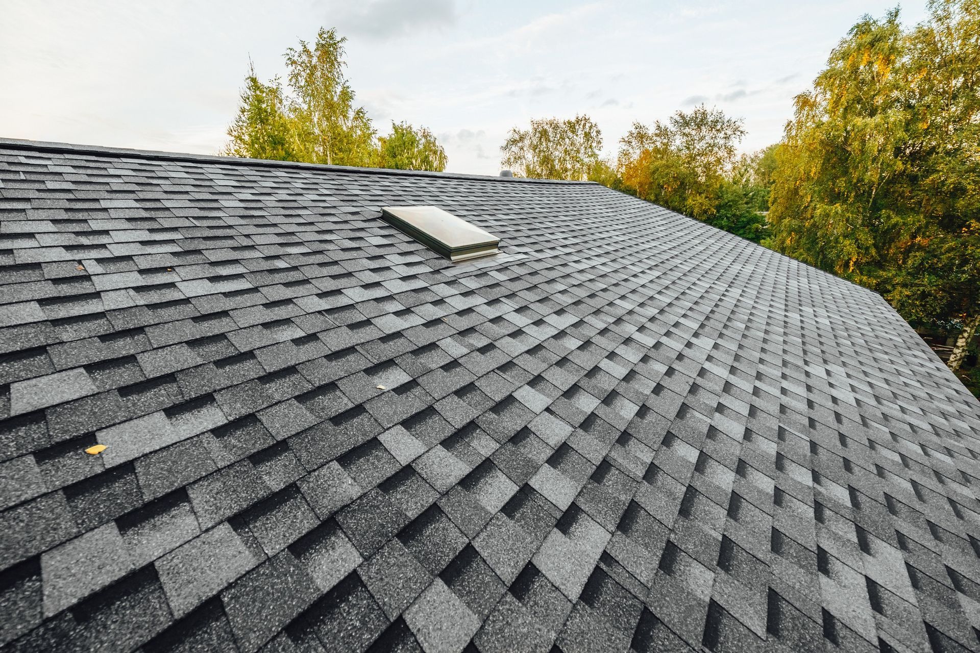 A close up of a roof with shingles and a skylight.