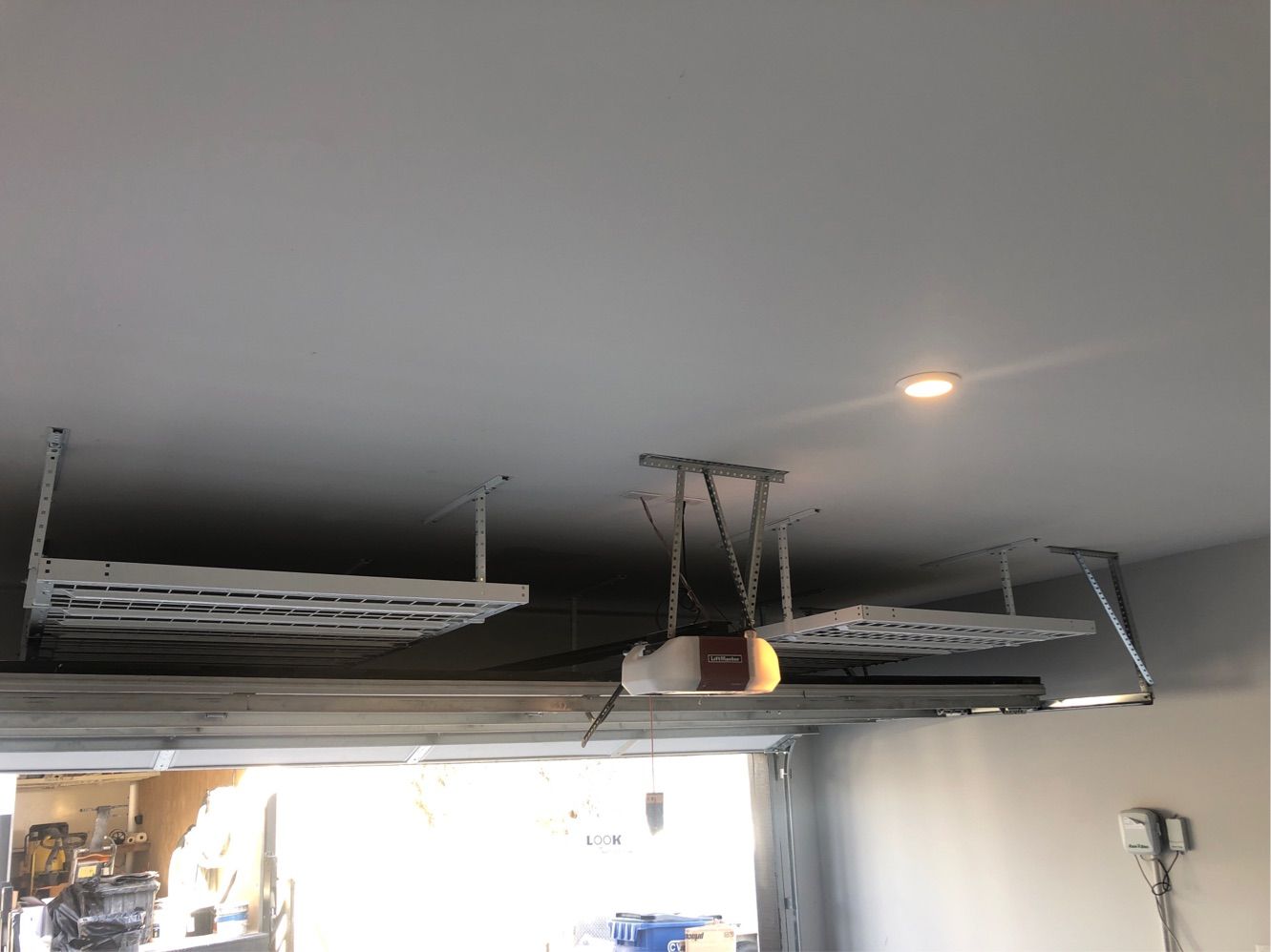 A garage with a garage door open and shelves hanging from the ceiling.