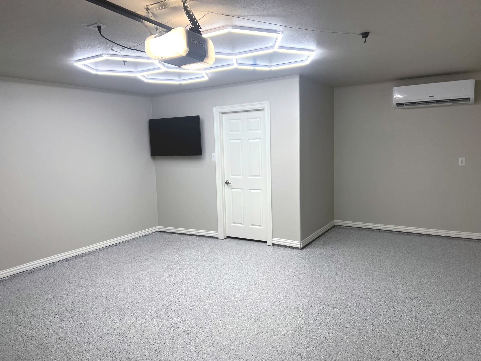 Empty garage with epoxy floor, TV, door, air conditioner, and a decorative ceiling light.
